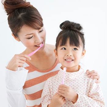 A woman and a girl are both holding a toothbrush and the woman looks on the girl and hold her on to the girl’s shoulder