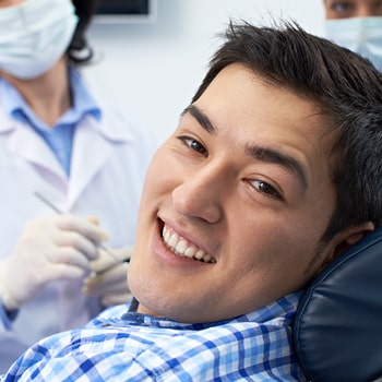  An Asian guys sitting on a dental chair wearing a Happy face looking at his left side 