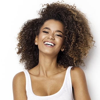 A lady with big curly hair and wearing a white top puts a laughing smile