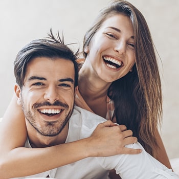 A long hair lady with a big laughing smile wraps her right arm to a smiling bearded man