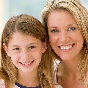 A smiling woman draws her face close to a smiling girl