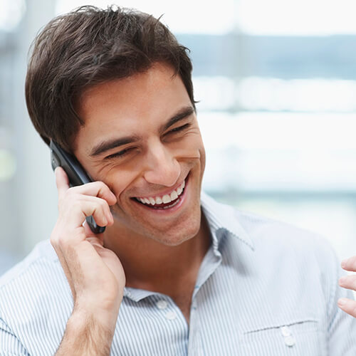 A smiling man is talking on his phone which he is holding with his right hand. 