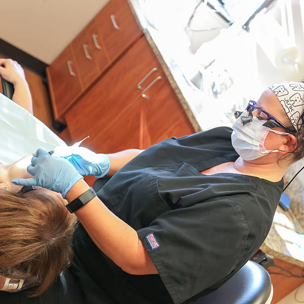 Team member  during a dental procedure to a woman lying in a dental chair