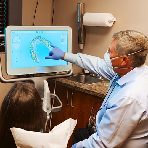 Dr. Mike Lakota points to the digital image of a tooth that needs a crown as a patient looks on.